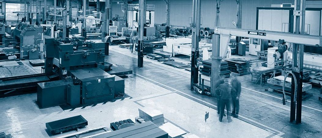 Eine weitläufige, modern ausgestattete Industriehalle in kühlem Blau-Grau-Ton, in der mehrere Mitarbeiter an verschiedenen Werkbänken und Maschinen der Dillinger Lochbleche arbeiten.