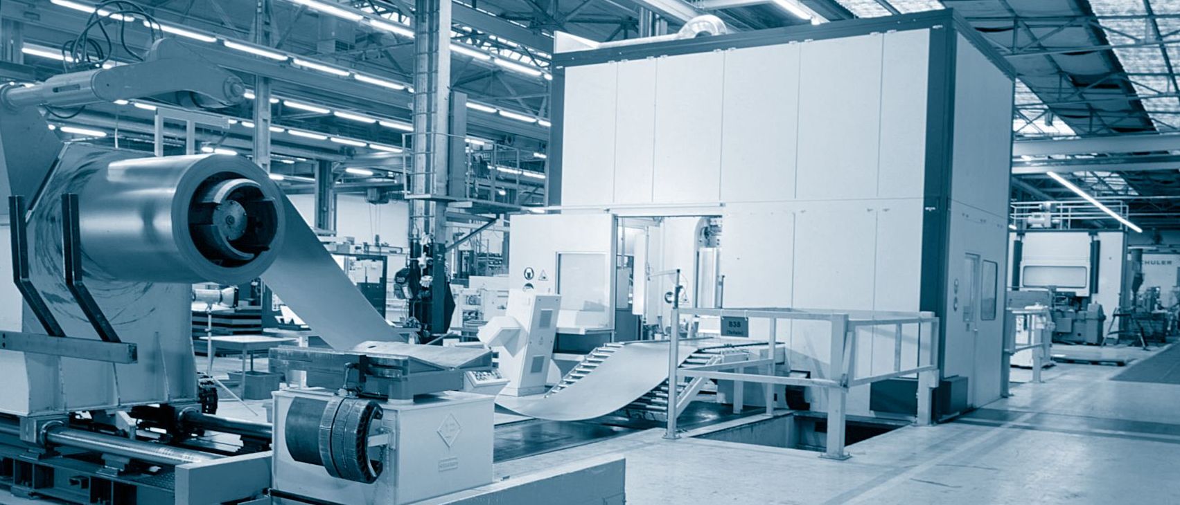 Eine helle, moderne Industrieanlage in kühlem Blau-Weiß-Look mit Fokus auf eine große, weiße Kabine oder Gehäuseeinheit und technische Fertigungsmaschinen in der Dillinger Fabrik gelochter Bleche.